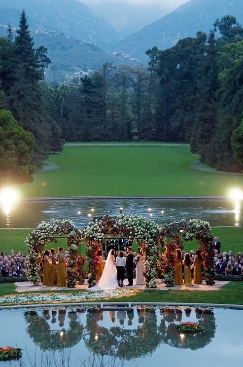 Hochzeit - As Dusk Falls, The Bride And Groom Exchange Vows Under A Flower- Laden Altar. As Dusk Falls, The Bride And Groom Exchange Vows Under A Flower- Laden Altar.