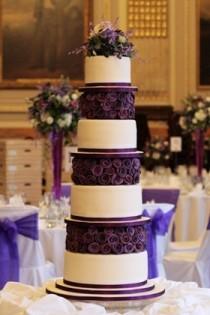 wedding photo - Layers Of Deep Purple Fondant Roses Contrast Against Tiers Of Sleek White Cake.